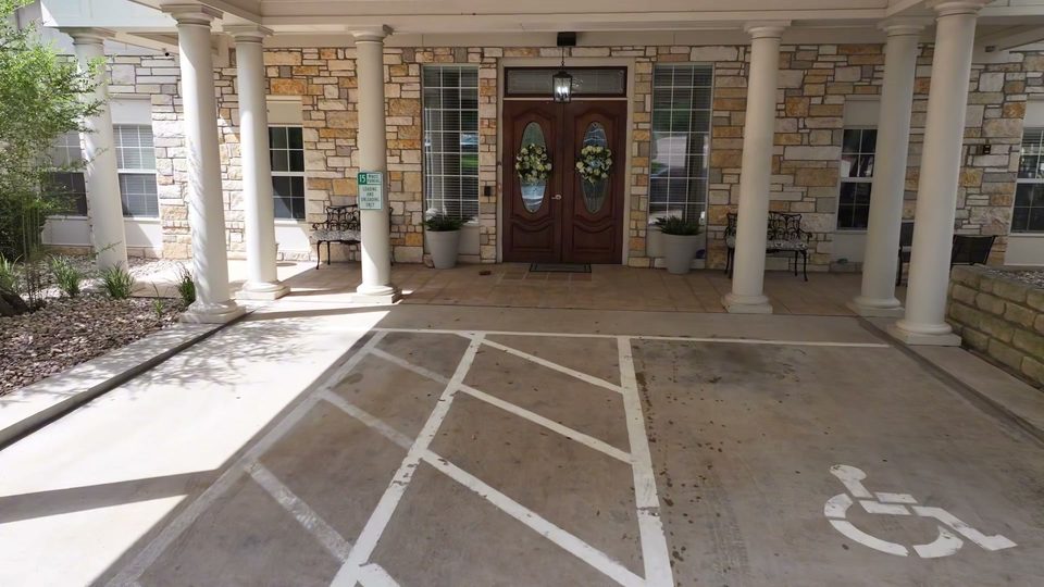 Covered entry at Bee Cave with limestone columns, wood doors, and an accessible space marked under the roof