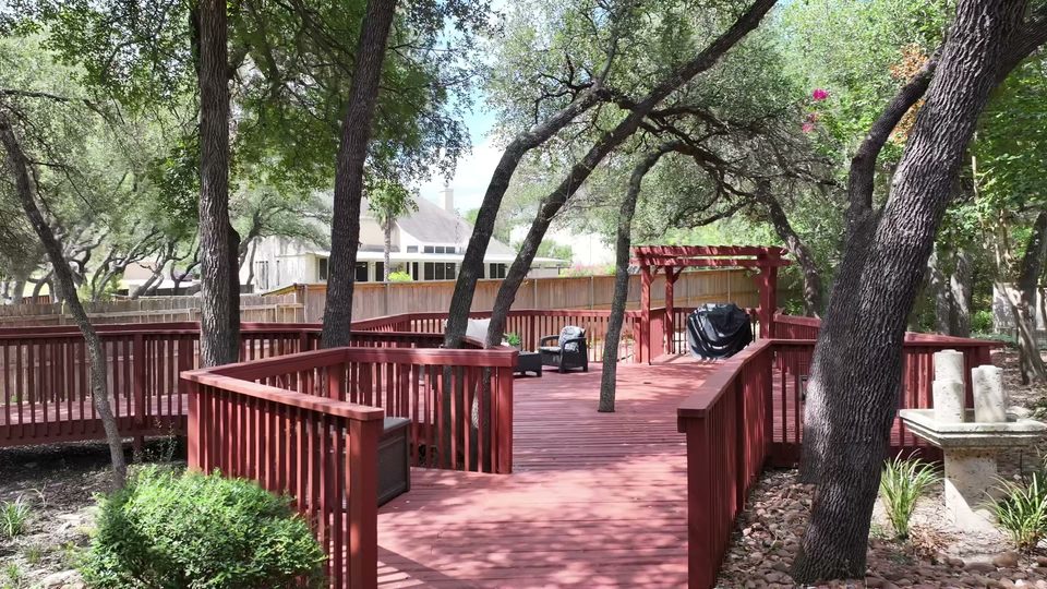 Wide back deck at Bee Cave built around live oak trunks, with a pergola at the far end