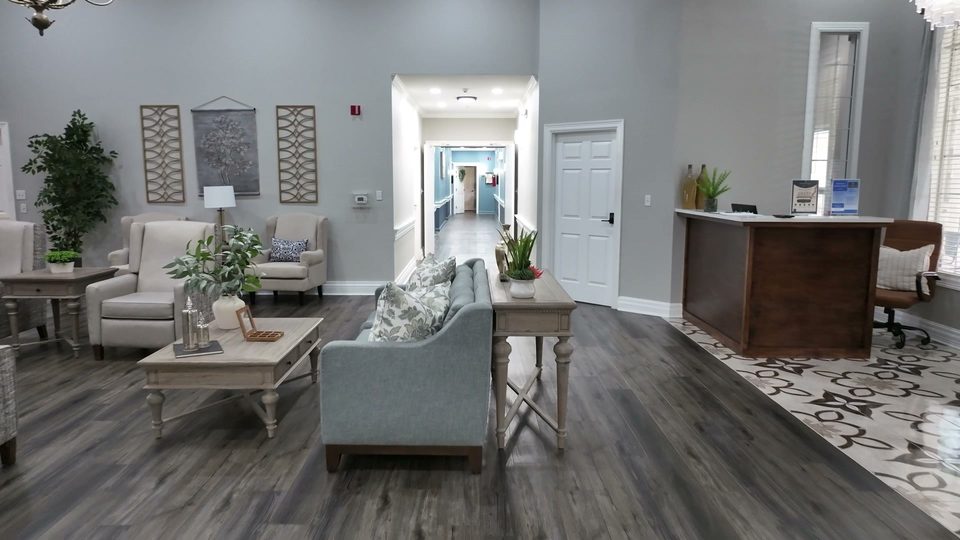 Sitting area at Bee Cave with a settee and side tables, the front desk beyond, and a hallway running back through the house