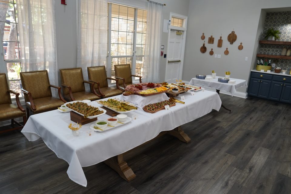 Dining room at Bee Cave with a long table of reception food, armchairs along the windows, and the servery beyond