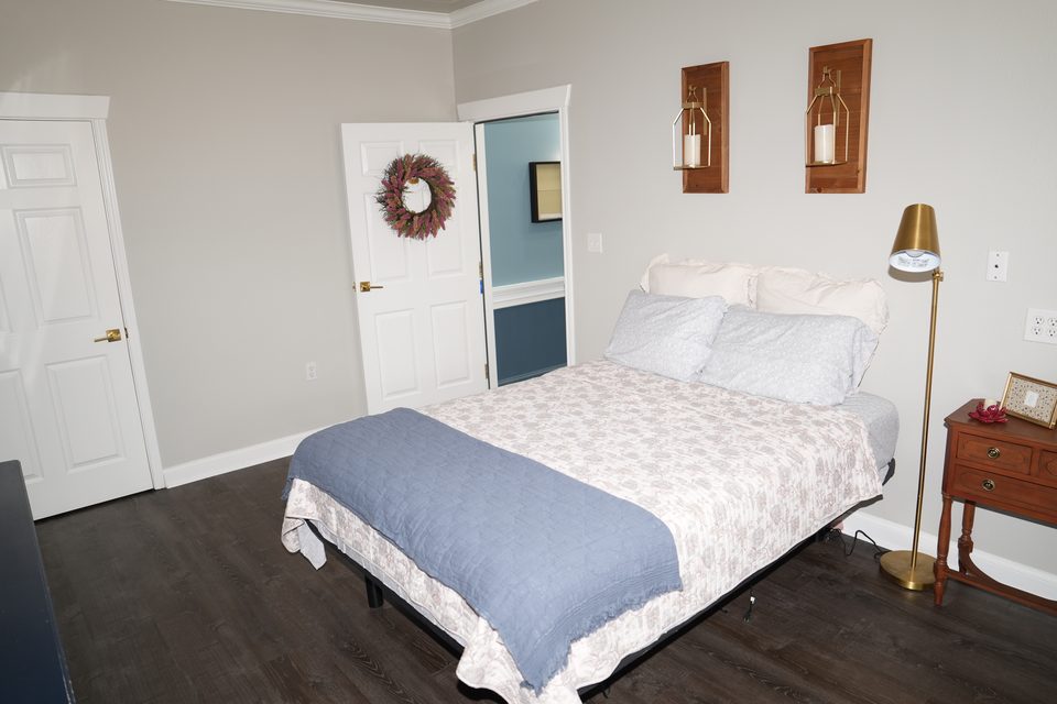 Private suite at Bee Cave with a made bed, wall sconces, a brass floor lamp, and the bathroom door standing open