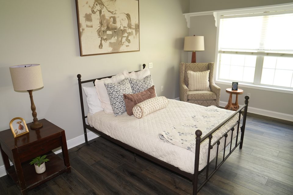 Private suite at Bee Cave with an iron bed frame, a framed print above it, and a wing chair by the window