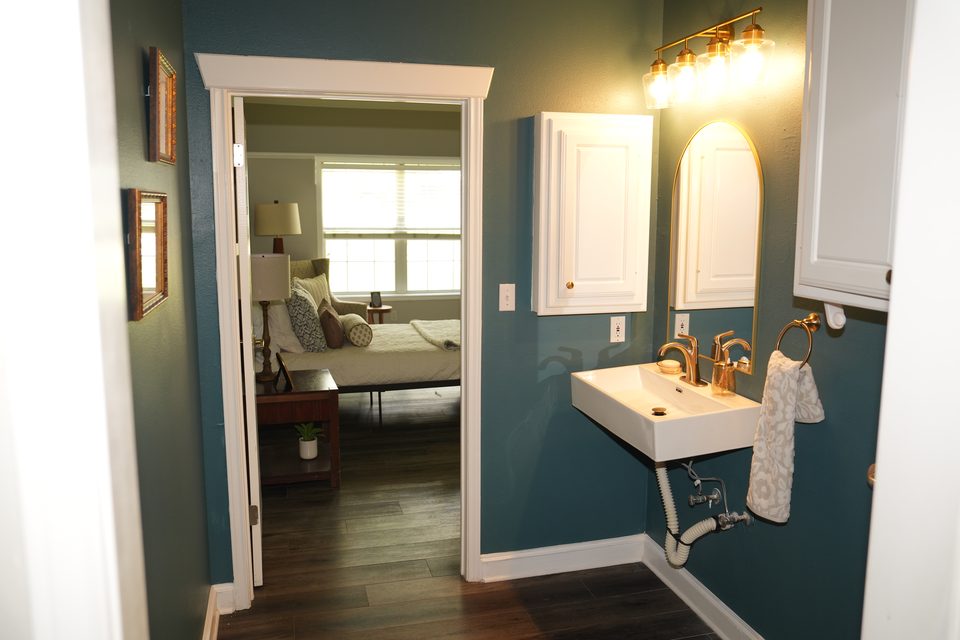 Private bathroom at Bee Cave with a wall mounted sink, an arched mirror, and the door open through to the suite